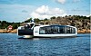 Hyke-passasjerbåt på vannet ved en steinete kyst med hytte i bakgrunnen