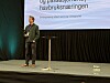 En mann står på en scene med mikrofon under en presentasjon foran et stort lerret.