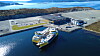 Et hvitt og gult prosessfartøy ligger ved kai foran et industriområde ved sjøen.