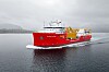 Rødt forskningsfartøy med dekksutstyr seiler på stille vann i grått vær.