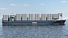 Et stort containerskip med mange stablede containere seiler på rolig sjø under klar himmel.