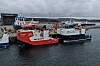 Rød og hvit ferge ligger ved kai sammen med andre fartøy i en havn.