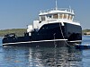 Et mørkt arbeidsfartøy med hvit overbygning ligger på rolig sjø.