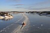 Lite fartøy i en åpen råk gjennom islagt vann, med bebyggelse langs kysten.